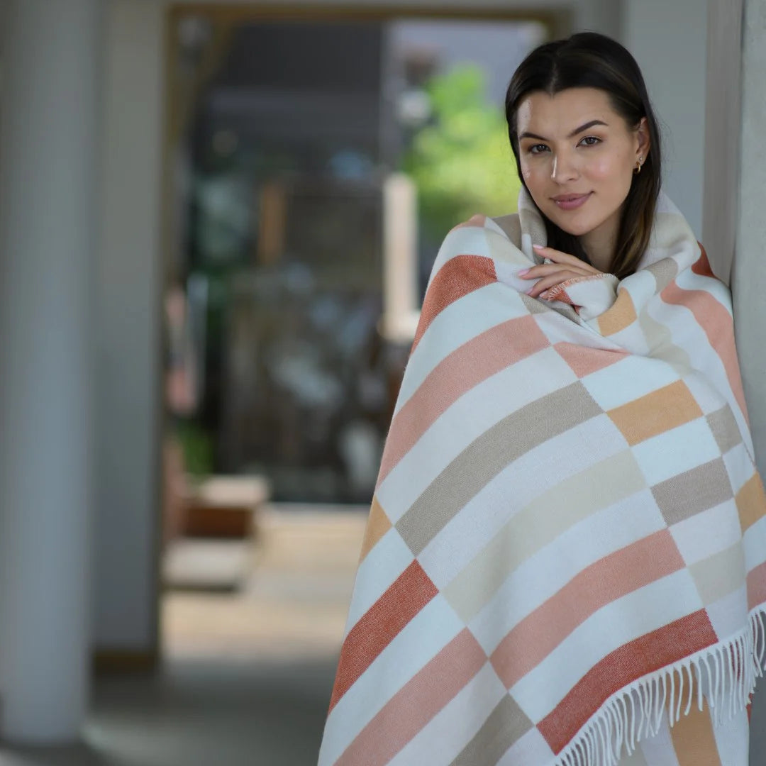 Woman wrapped in a Bella Vita Sequence Cinnabar/Dark Beige throw in a blurred indoor setting