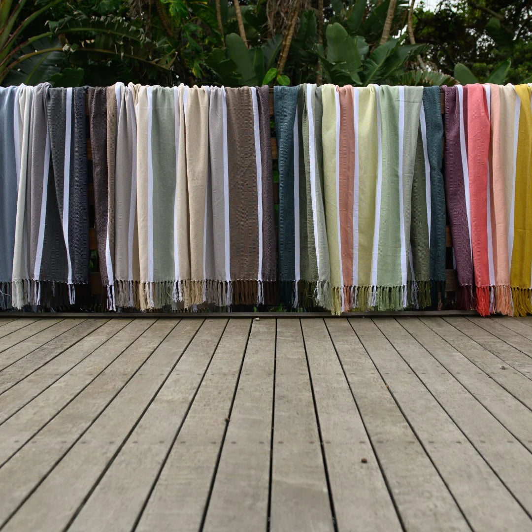 Protea Pinstripe Sunset throw - striped design with hand-knotted fringes. hanging on a wooden deck with a garden background