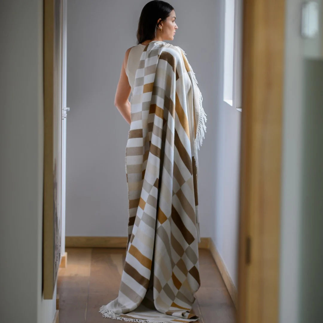 Woman draped in a Bella Vita Sequence Coffee/Cobblestone throw standing in a room with neutral walls and wooden flooring.