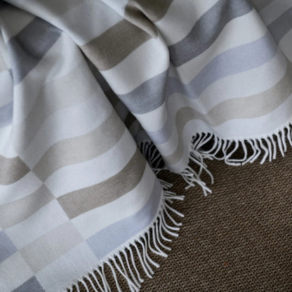 Bella Vita Sequence Wild Dove/Oyster Grey throw with fringes on a textured surface