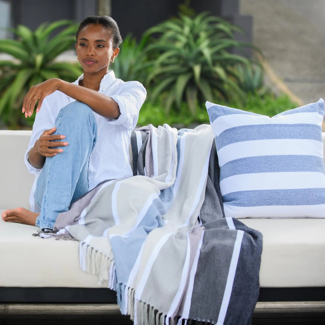 Woman sitting on a couch with Protea Chenille Scatter Cushion in Overcast Sky and White, and a blanket in an outdoor setting