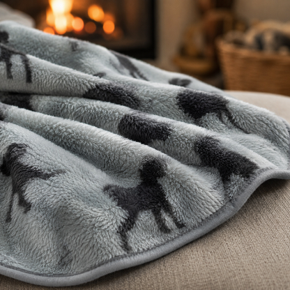 Grey pet blanket with black dog patterns on a couch in a cosy room.